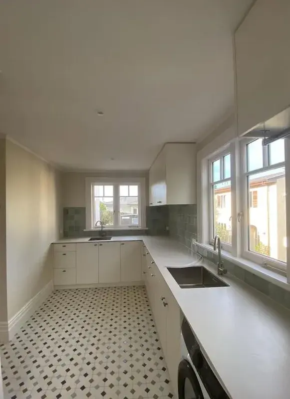 Bright white painted kitchen with green tile splashback and patterned floor