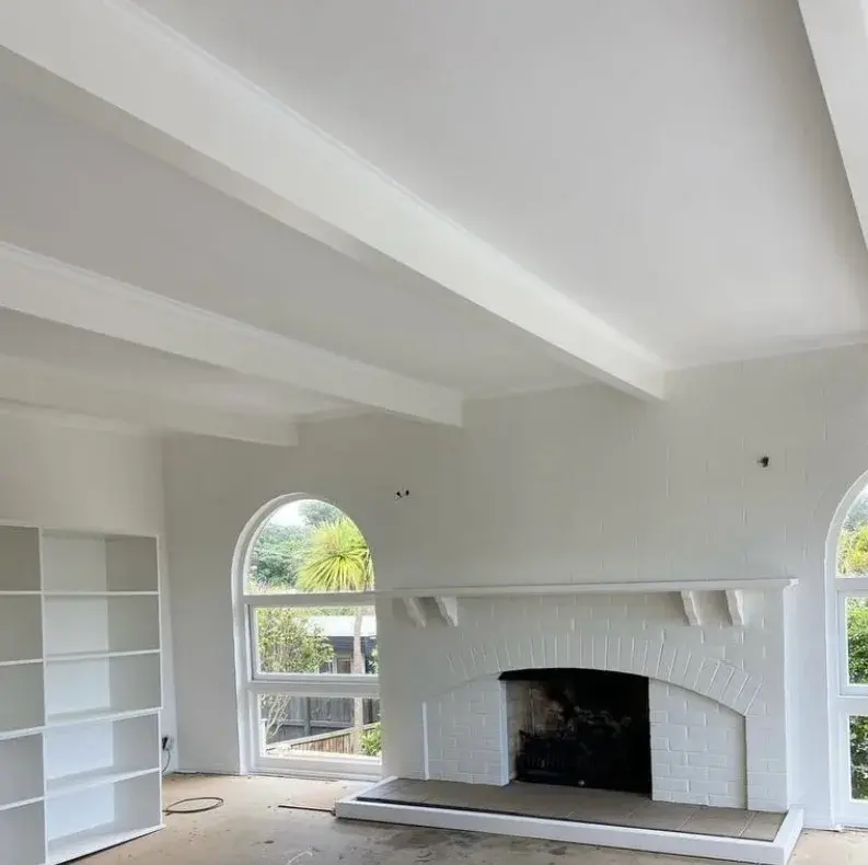 Bright white painted living room with brick fireplace, ceiling beams and arched windows