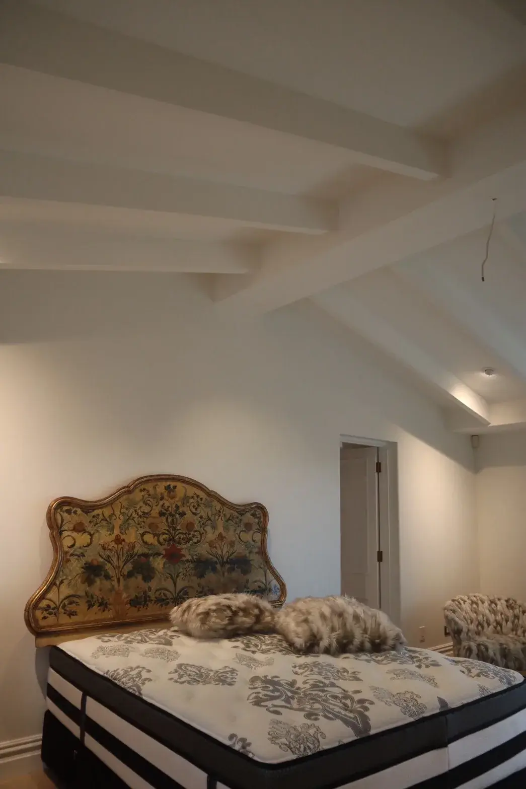 Heritage Auckland master bedroom with white painted vaulted ceiling and exposed beams above an antique headboard