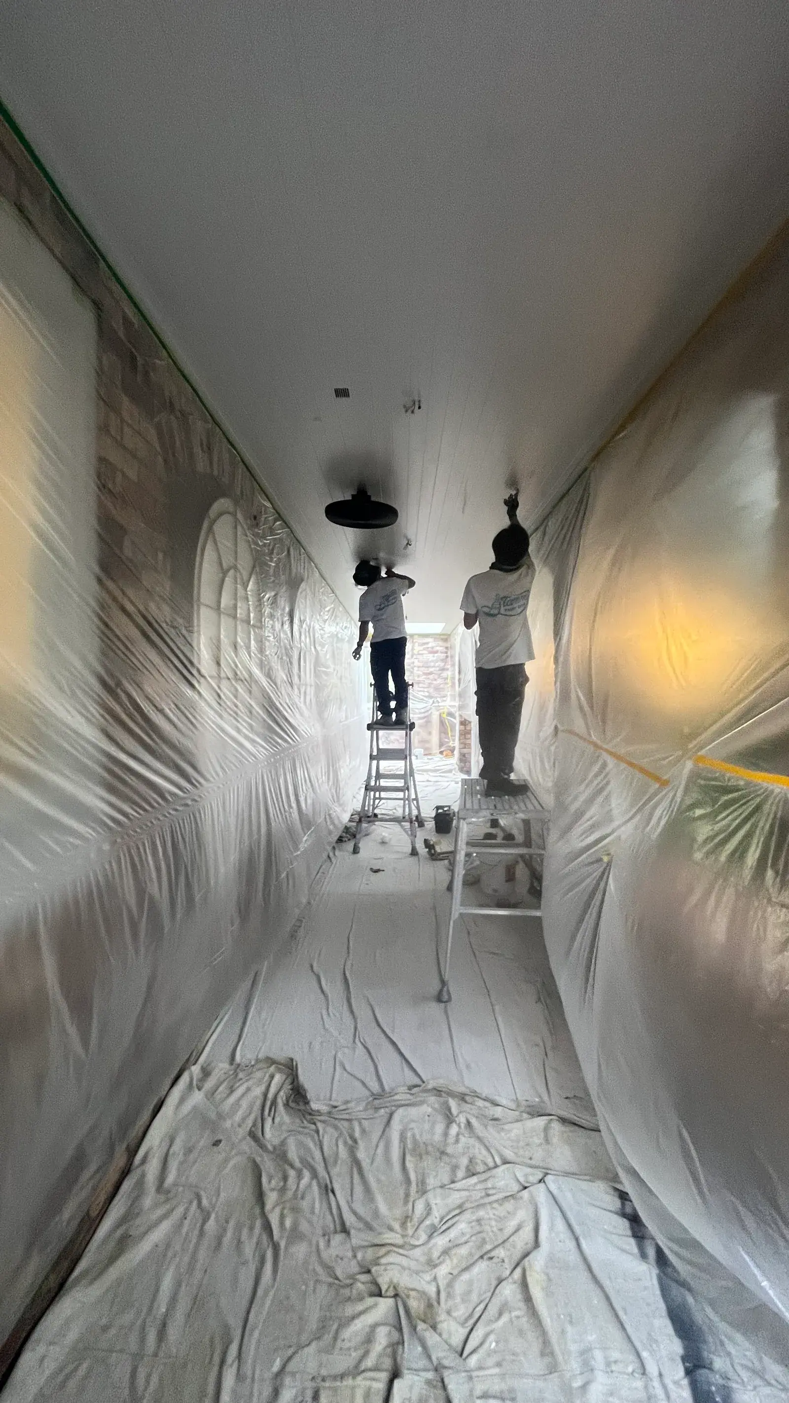 Tommy Paint Redo crew on ladders painting a fully masked hallway ceiling in Auckland
